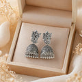 Antique silver jhumka earrings with deity motif, anti-tarnish finish, displayed in luxury gift box