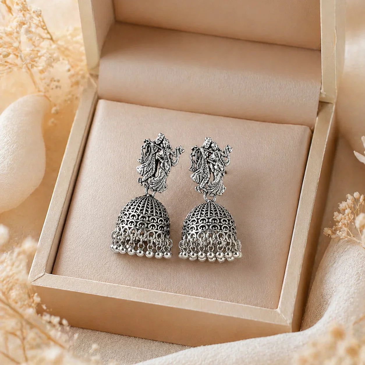 Antique silver jhumka earrings with deity motif, anti-tarnish finish, displayed in luxury gift box