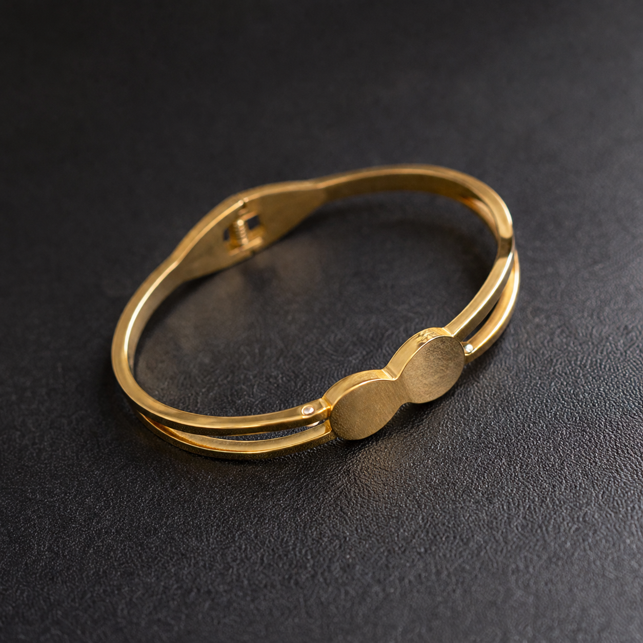 Gold tone anti-tarnish bangle bracelet with sleek double-bar design and subtle crystal accents on dark texture.