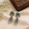 Peacock eye jhumka earrings with green enamel, silver filigree, and dangling bells on soft fabric