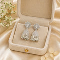 Elegant silver jhumka earrings with floral studs, displayed in a velvet box on satin fabric with delicate flowers.