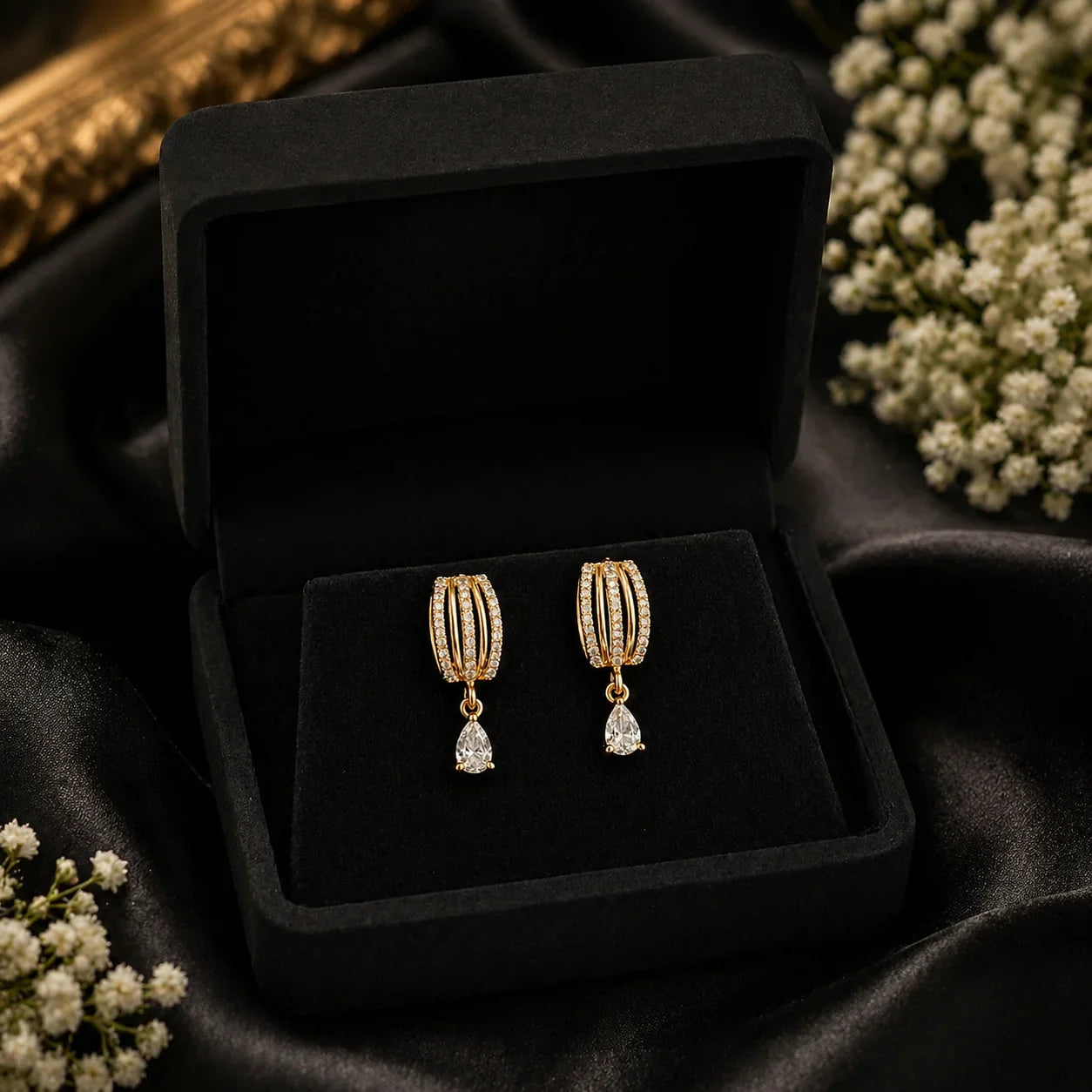 Elegant gold hoop earrings with pear drop crystals, displayed in black velvet box with white flowers