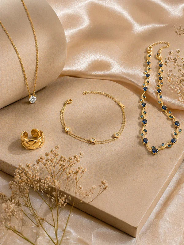 Elegant gold jewelry set with diamond pendant, sapphire necklace, and textured ring on satin